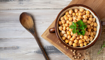 A bowl of boiled chickpeas, parsley and a wooden spoon on the rustic table. The view from the top.