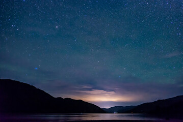 Fototapeta na wymiar starry sky above the shape of mountains with the light of a city in a fjord in the Marlborough Sounds, New Zealand