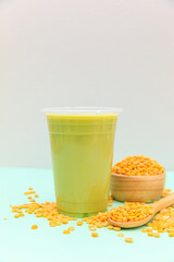 Soy milk mix green tea in glass and soybean on spoon on table background, health concept