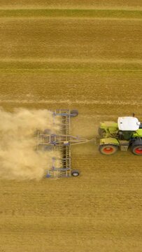 Tractor plowing field. Aerial view of moving tractor with plow raising dust. Tractor plows ground on cultivated farm field. Aerial vertical,&nbsp;vertical video background. 