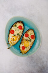 Baked eggplant with cheese, egg and tomatoes on a blue plate on a gray background.