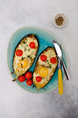 Baked eggplant with cheese, egg and tomatoes on a blue plate on a gray background.