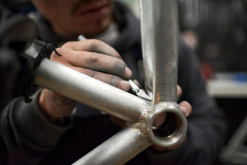 Hands of an unrecognizable hispanic man removing paint residue from a bicycle frame as part of the...