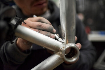 Hands of an unrecognizable hispanic man removing paint residue from a bicycle frame as part of the process of a bike renovation work made at his workshop. Composition with selective focus.