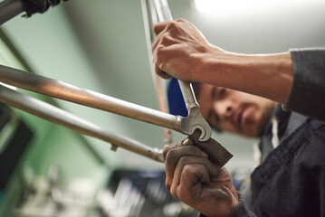 Latin man sanding an unpainted bicycle frame as part of the process of a bike renovation work made at his workshop. Composition with selective focus on the hands.