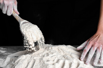 Baker pouring flour with a spoon on kitchen table. Preparing dough for bread. Baking concept.