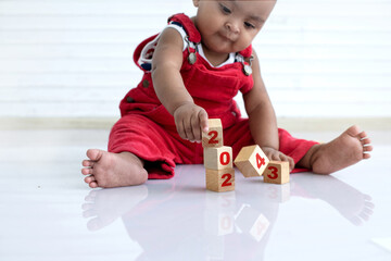 African baby girl in red cloth sitting on floor playing with wooden blocks, wooden blocks with 2024...