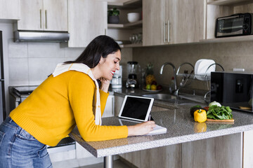 Latin adult woman cooking and writing recipe in a notebook in kitchen at home in Mexico, Hispanic female preparing mexican food in Latin America