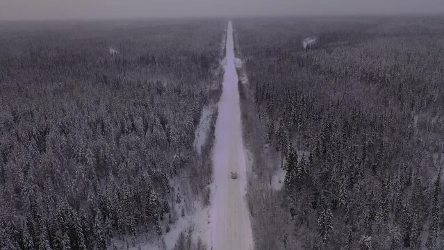 The car is moving on a snowy road. Landscape of winter taiga. Russian winter of northern latitudes from a drone.