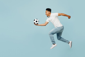 Fototapeta na wymiar Full body side profile view happy young man fan wear t-shirt cheer up support football sport team jump high hold catch soccer ball watch tv live stream isolated on plain pastel blue color background.