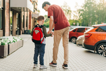 Happy father and kid son going to classes. Parent take child boy to school in first grade. Pupil of primary school go study with backpack outdoors in city street. Beginning of lessons. Back to school.