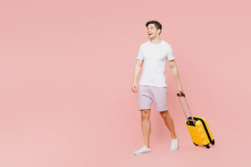 Traveler side view man wear summer casual clothes hold suitcase walk go isolated on plain pink background studio. Tourist travel abroad in free spare time rest getaway Air flight trip journey concept