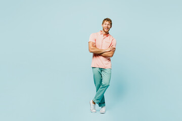 Fototapeta na wymiar Full body young caucasian blond man he wears pink t-shirt casual clothes look camera hold hands crossed folded isolated on pastel plain light blue cyan background studio portrait. Lifestyle concept.