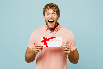 Young surprised blond man he wear pink t-shirt casual clothes hold gift certificate coupon voucher...