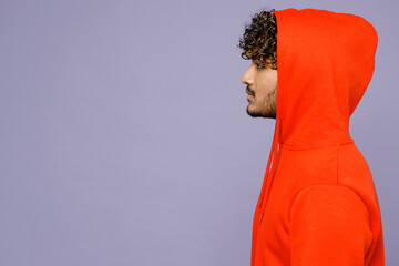 Side view young unshaven cool serious student Indian man in hood wear red orange hoody casual...