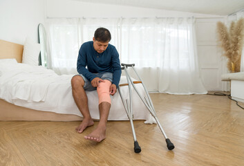 A man with a broken knee sitting on his bed. He leans on crutches, signalling recovery from injury....