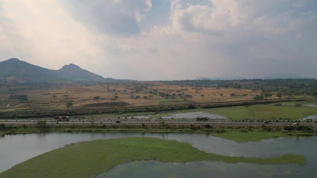 Vehicles driving Mumbai-Nashik highway over river and mountain in the horizon, Nashik 4K aerial drone shot