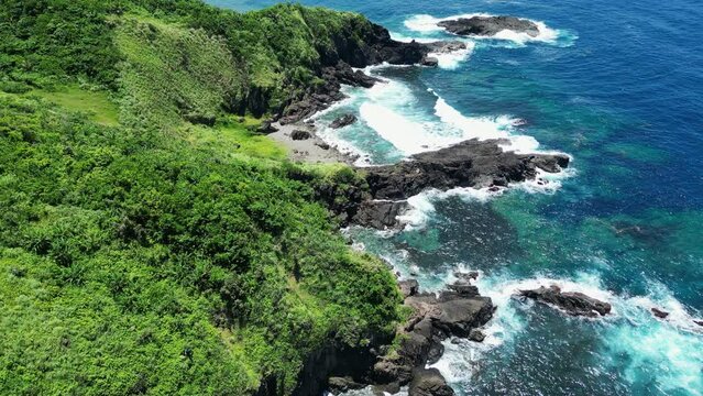 Jagged rocky basalt coastline with powerful waves whitewash crashing on green shores