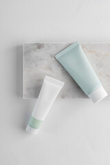 white and green cosmetic tubes on a white background on marble tray. The concept of a cream with natural ingredient and not testing on animals.