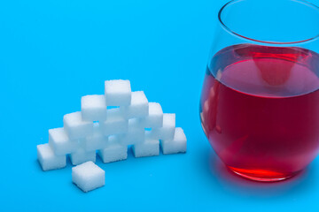 Zbliżenie na szklankę soku owocowego z dodatkiem niezdrowego białego cukru w kostkach 