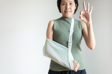 Woman showing ok sign and wear sling for recovery broken arm on white background