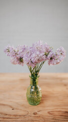 Light purple coloured flowers in a glass vase on a wooden table with grey wall at background