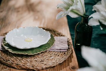 A ceramic plate placed on a coaster  with a beautiful white lily in a glass vase on a wooden table