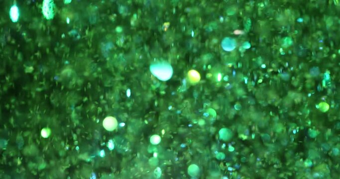 Green glitter background in magic dust and shiny green texture. Festive lights flying particles form beautiful bokeh