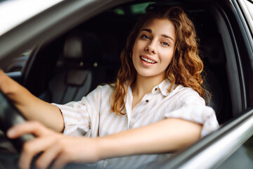 Fototapeta na wymiar Beautiful smiling woman driving a car. The driver is a woman driving. Summer outdoor portrait. Car travel, lifestyle concept.