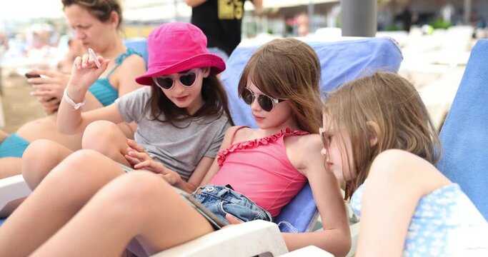 Three child girls with tablet on beach lie in sun lounger. Children applications and children bloggers in summer on beach