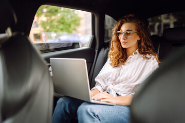 Business woman works in the back seat of a car with a laptop during a taxi ride. Business concept, blog, freelancing.