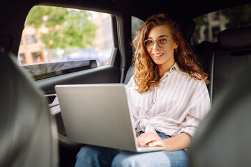 Business woman works in the back seat of a car with a laptop during a taxi ride. Business concept, blog, freelancing.
