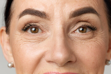 Closeup portrait of middle aged woman face with brown eyes over grey background. Model looking at camera. - obrazy, fototapety, plakaty