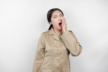 Portrait of sleepy Asian woman wearing a brown uniform and covering her mouth with a hand while...