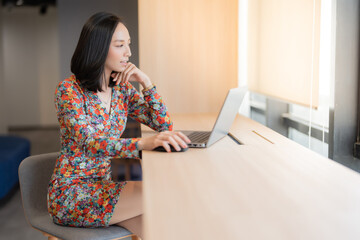 Half body portrait of Asian female executives Head of a company department, short hair, working on a laptop at his desk. By the window in the home office about business wearing a beautiful floral suit