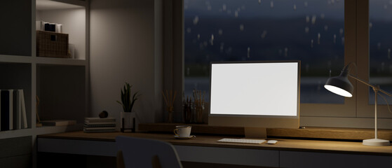 A modern, dark home workspace with a computer on a desk against the window on a rainy night.