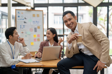 A successful Asian male CEO or businessman sits on a table with a coffee cup in his hand