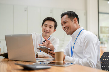 Fototapeta na wymiar Two cheerful Asian male bankers are looking at a laptop screen and working together