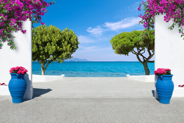 view to the mediterranean sea with white wall, potted blooming flowers, bougainvillea and trees in Greece