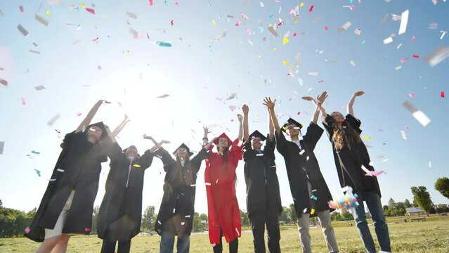 Happy college graduates throw colorful confetti against the rays of sunshine.