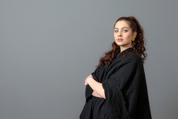 Naklejka premium portrait of charming curly-haired woman in a black cloak isolated on a gray background