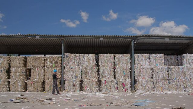 Stacked pressed bales recycled waste paper under cover with laborer walking past