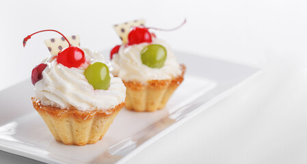 Beautiful cream cakes with cherries and grapes on a plate on a white background