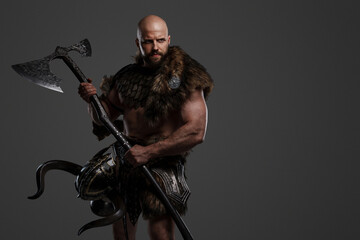 A strong and intimidating Viking man in a beard and bald head, dressed in animal fur and light...