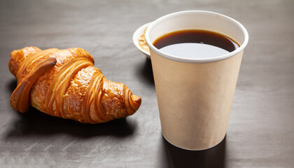 Aromatic coffee in a paper cup paired with a flaky croissant. With copy space