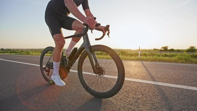 Focus on light carbon road bike with drop handlebars being ridden fast on smooth highway in summer evening. Professional cyclist enjoying miles in saddle while exploring rural area outdoors.