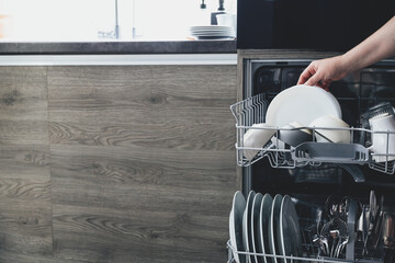 Close-up view of female woman hand unloading dishes, empty out or taking white plates, dishes from...
