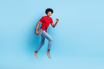 Fototapeta na wymiar Full size photo of handsome guy dressed red stylish t-shirt denim pants hold laptop run to empty space isolated on blue color background