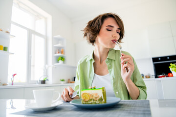 Photo of dreamy adorable lady dressed green shirt closed eyes eating tasty pie indoors house kitchen
