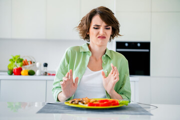 Photo of sad moody lady dressed green shirt dislike vegetables plate having toxicosis indoors house kitchen